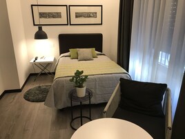 A neatly arranged hotel room with a bed, a bedside table with a lamp, a small round table, and a potted plant.