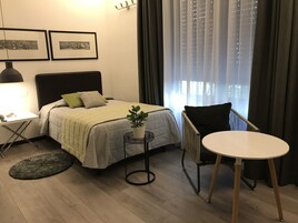 Una camera da letto ordinata con un letto, un comodino, una lampada, una sedia e un tavolino con una pianta.