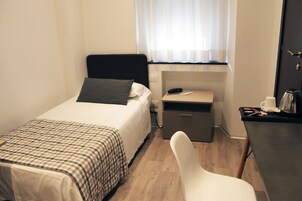 Un dormitorio pequeño y ordenado con cama, mesita de noche, silla y escritorio con lámpara.