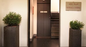 A hotel entrance with a dark wooden door, a staircase, and two potted plants. - Kursaal and Ausonia Hotel (Florence)