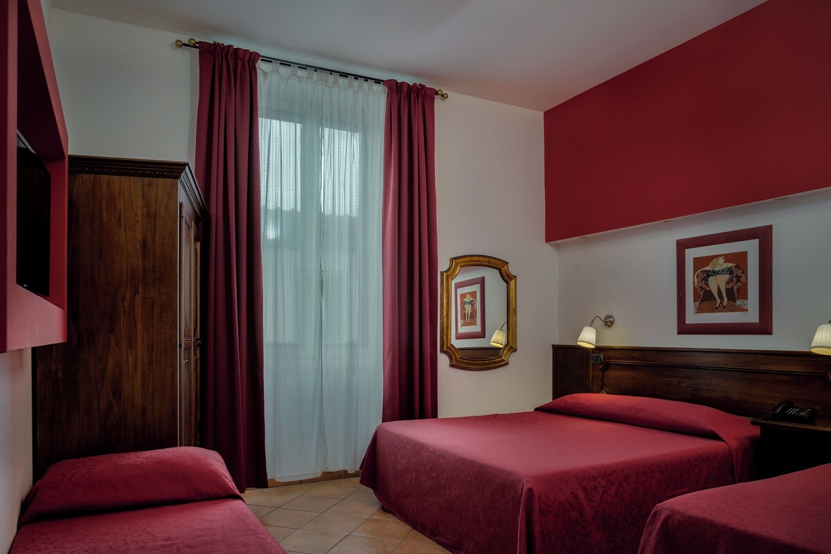 A hotel room with two beds, a wooden wardrobe, a mirror, and a framed picture on the wall.