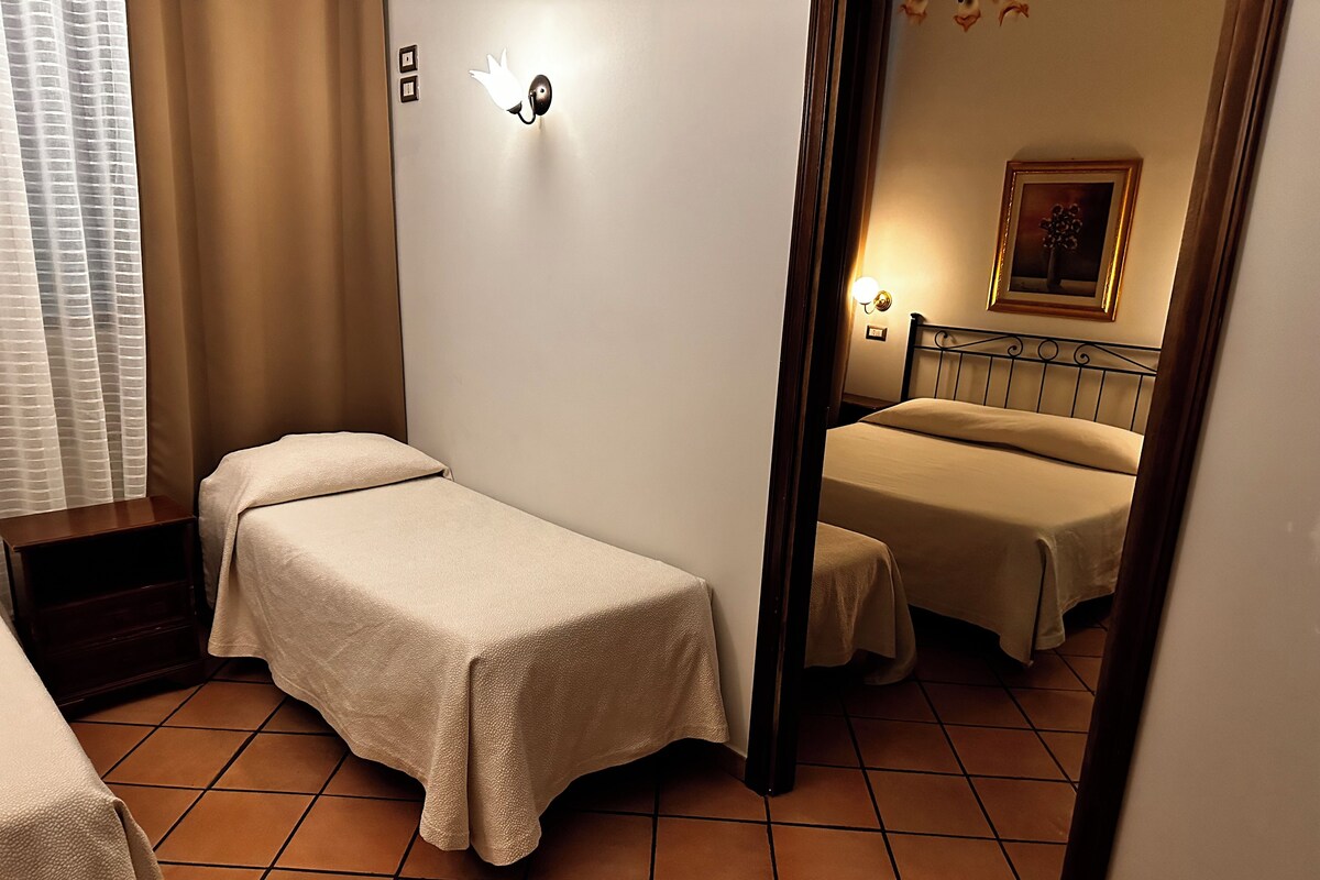 A hotel room with a single bed, a second bed, a nightstand, a mirror, and a wall-mounted light fixture.