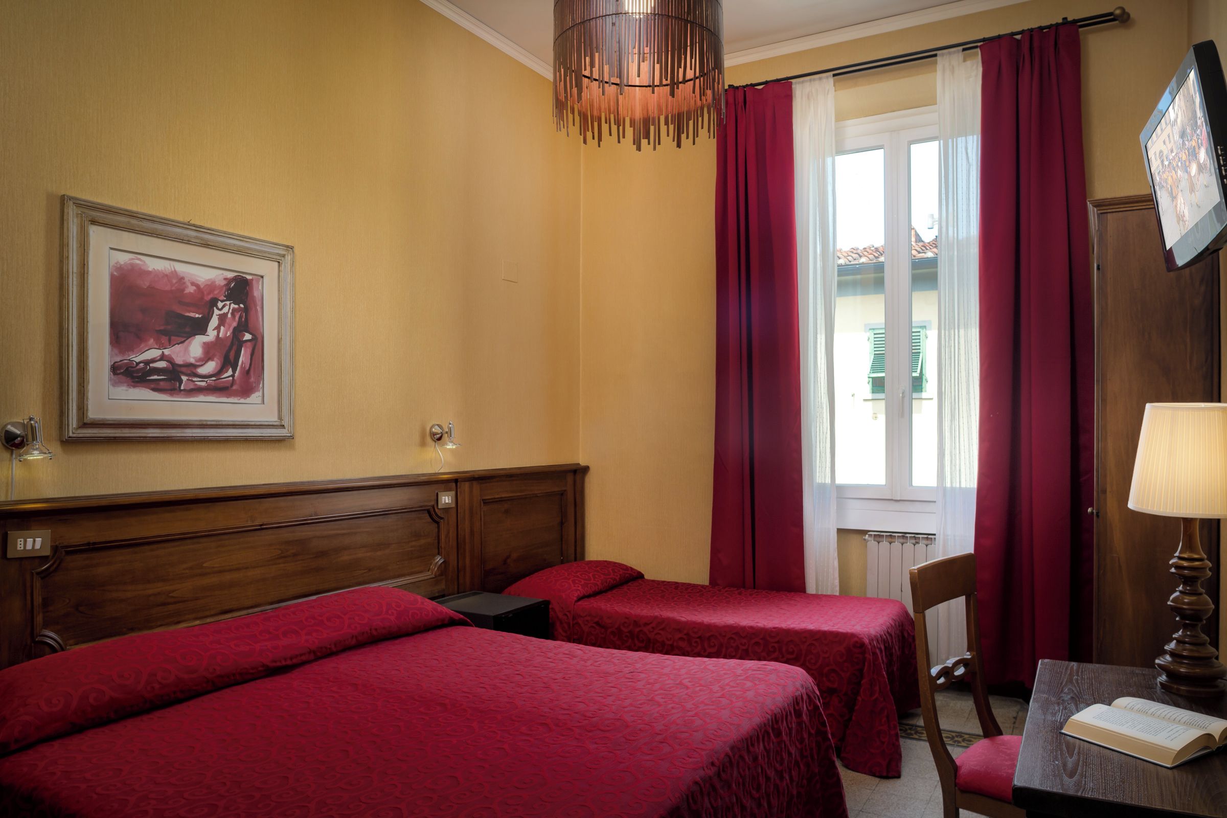 A hotel room with two beds, a painting on the wall, a window with curtains, and a lamp on a table.
