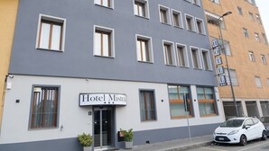 Um hotel moderno com uma placa indicando "Hotel Mistral". Possui várias janelas, uma entrada visível e um carro estacionado na rua.