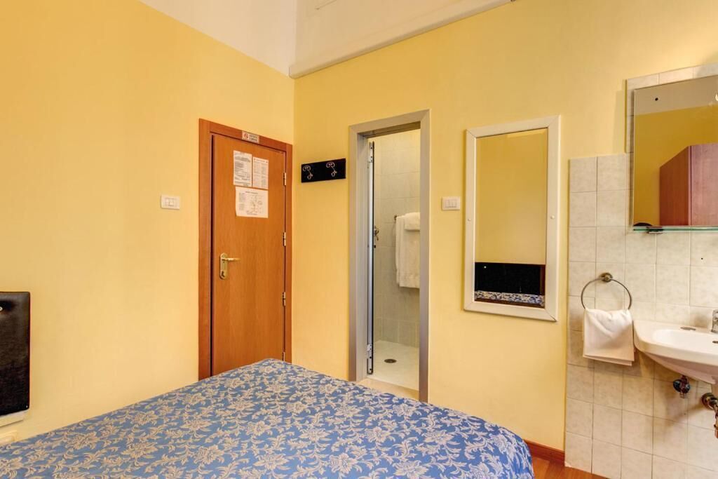 A bedroom with a bed, a door, a shower, and a bathroom with a sink and mirror.