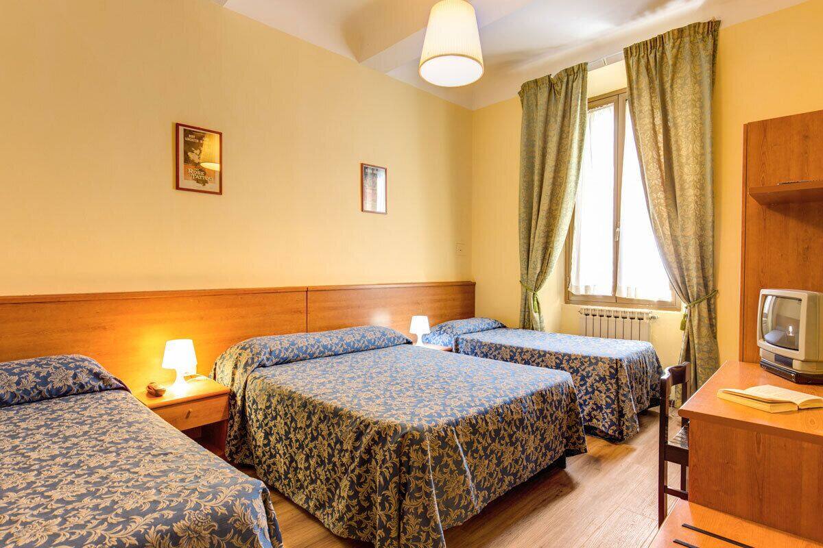 A hotel room with two beds, a wooden headboard, a television, and a window with curtains.