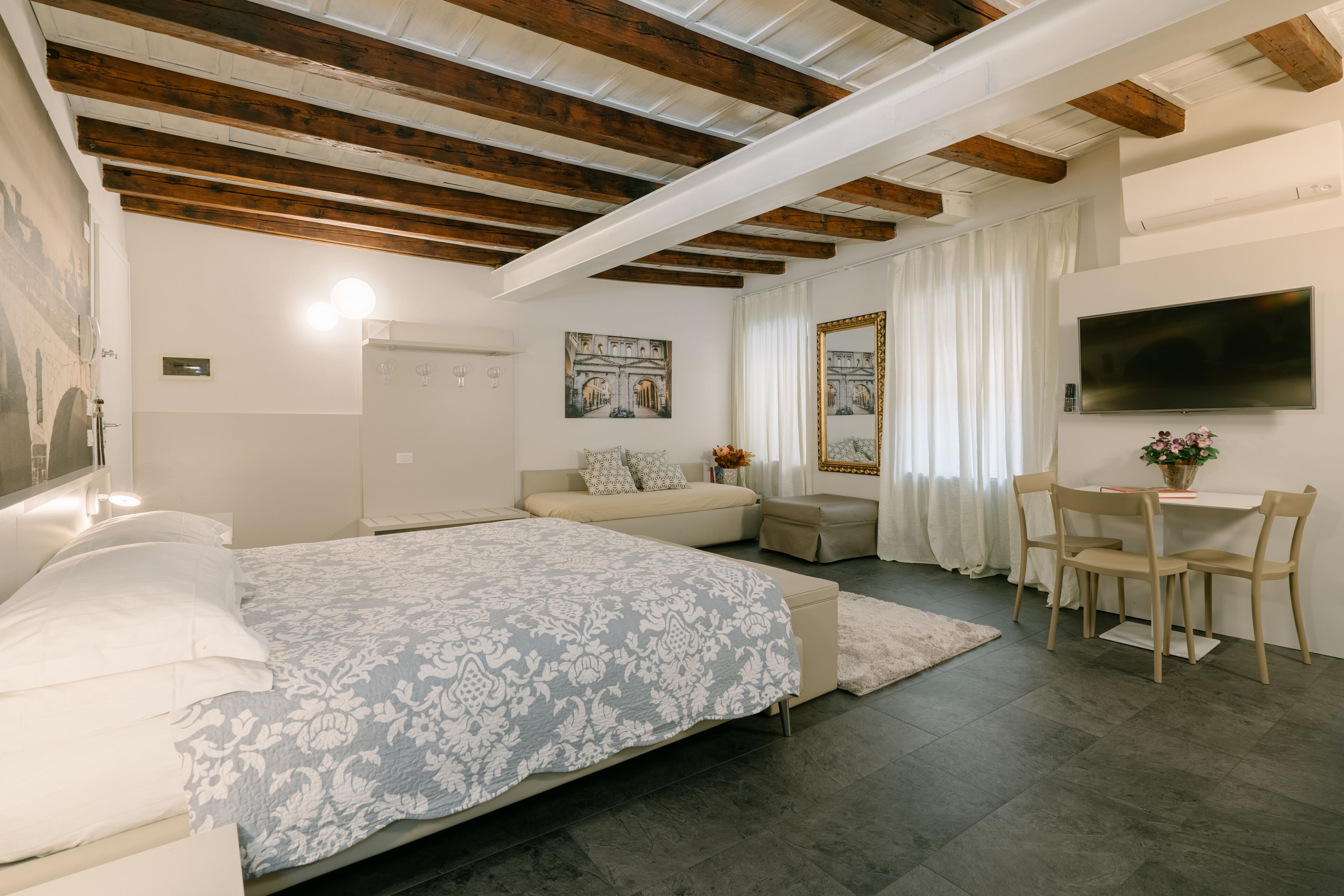 Une chambre à coucher avec un grand lit, un bureau avec deux chaises, une télévision et des œuvres d’art accrochées aux murs.