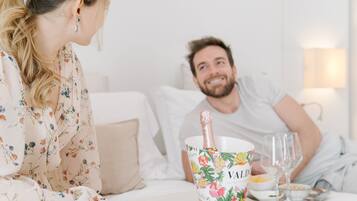 Una habitación con una cama, una mesita de noche con una botella de champán, un bol de comida y una copa.