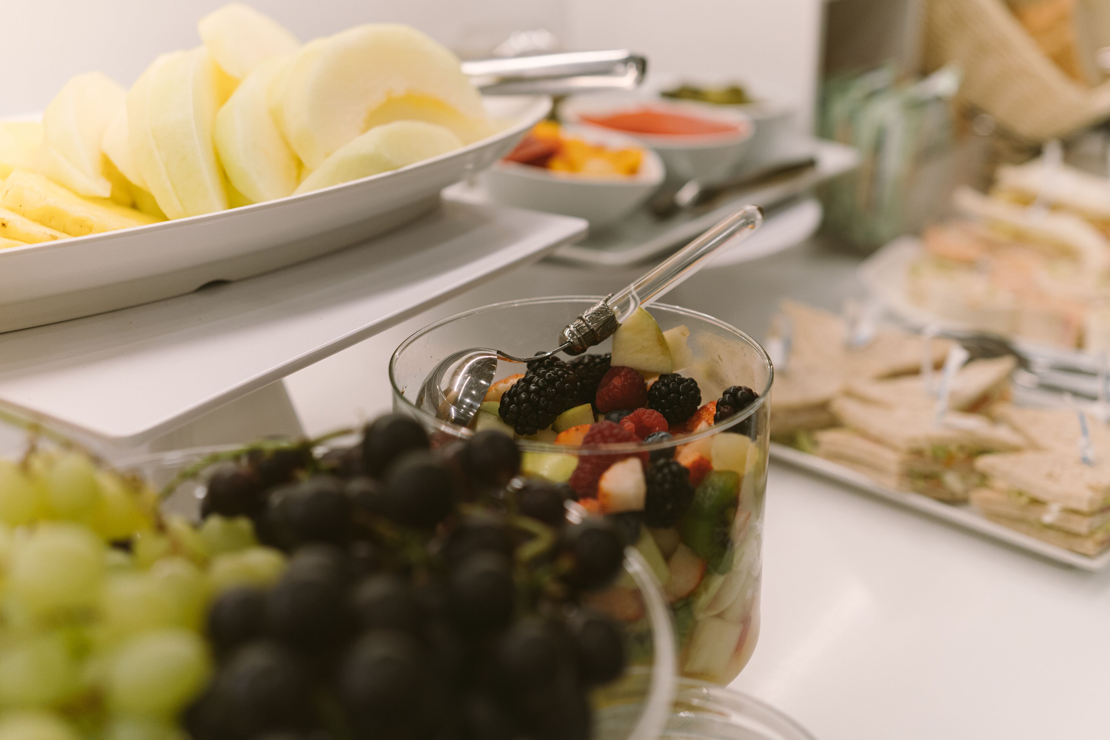 A buffet table with various food items including sliced apples, a fruit salad, and sandwiches.