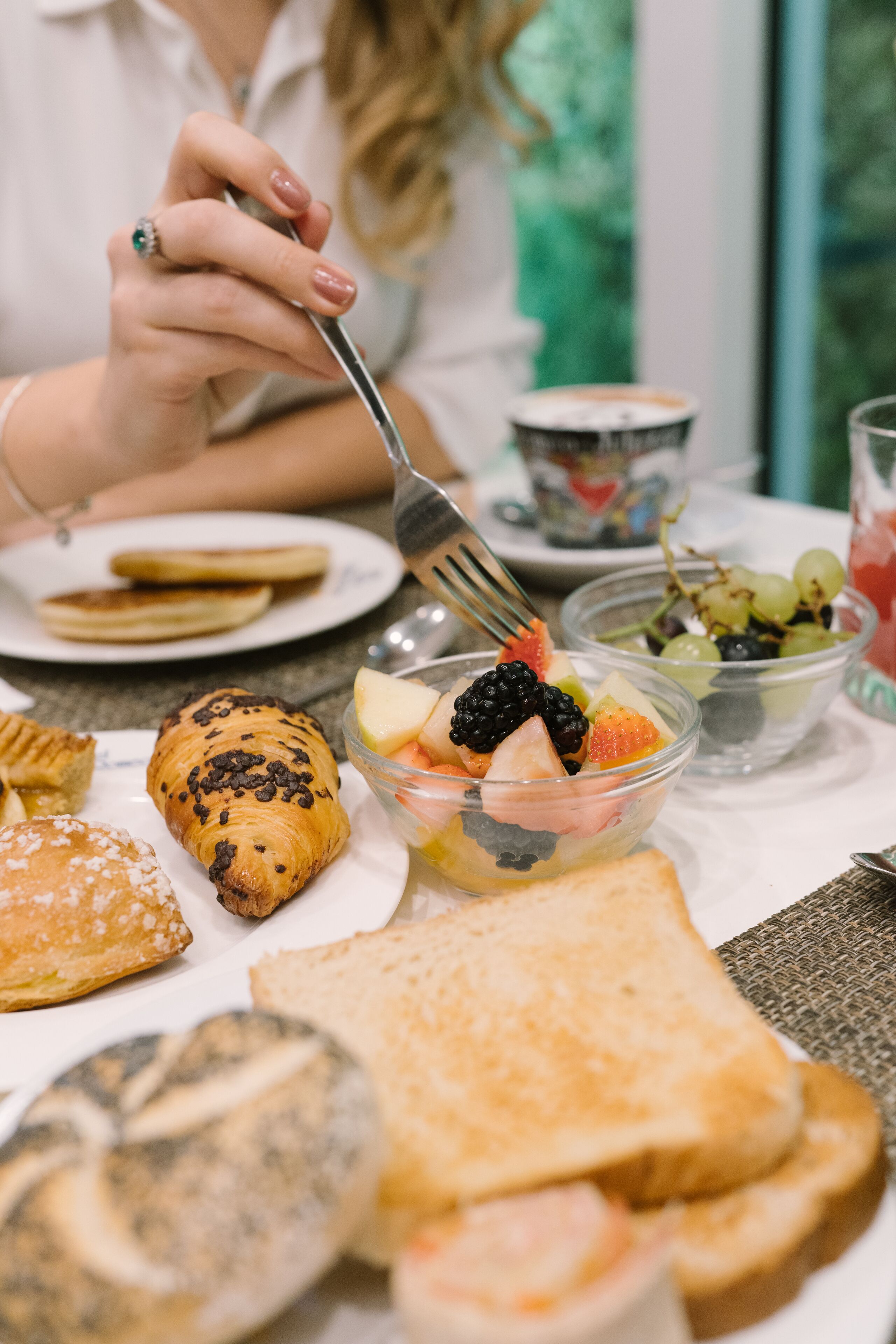 Un desayuno con varios pasteles, fruta y tostadas sobre una mesa.