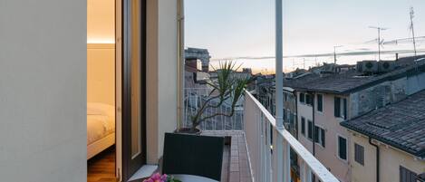 A balcony with a bed, a table with a potted plant, and a view of the cityscape.