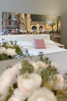 A bed with a pink pillow, white bedding, and a floral arrangement in the foreground.
