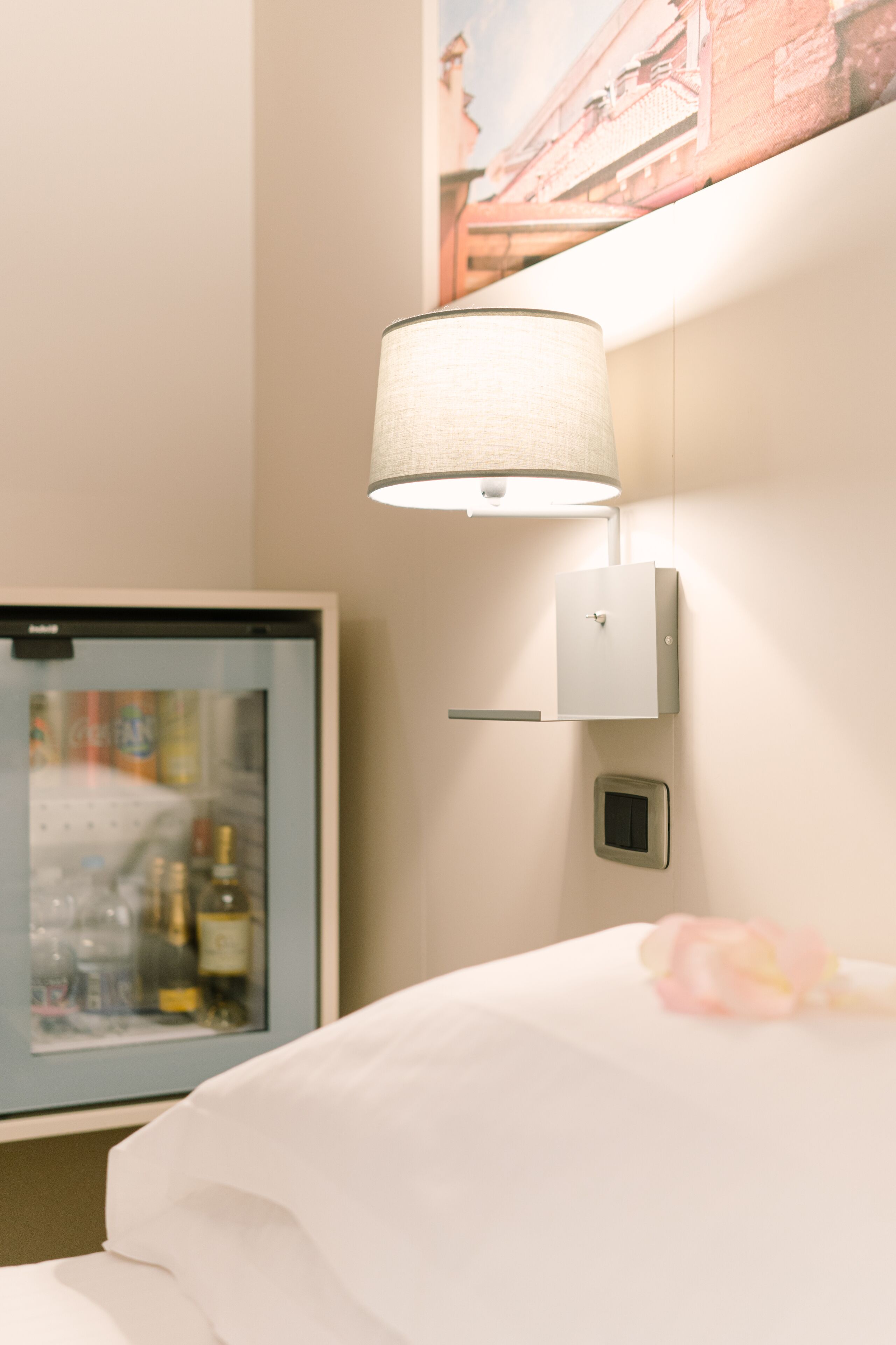 Quarto de hotel com cama, luminária na parede, televisão e quadro emoldurado.