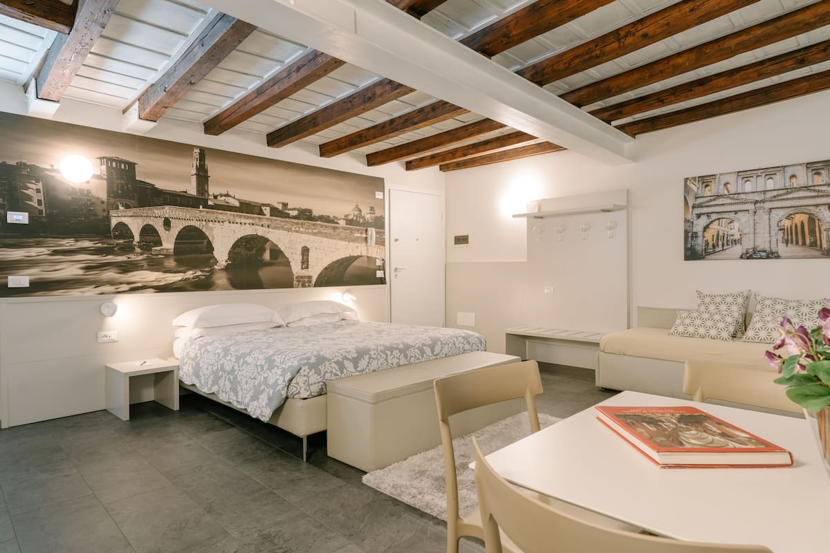 A modern bedroom with a bed, a small table, a sofa, and a wall-mounted shelf.