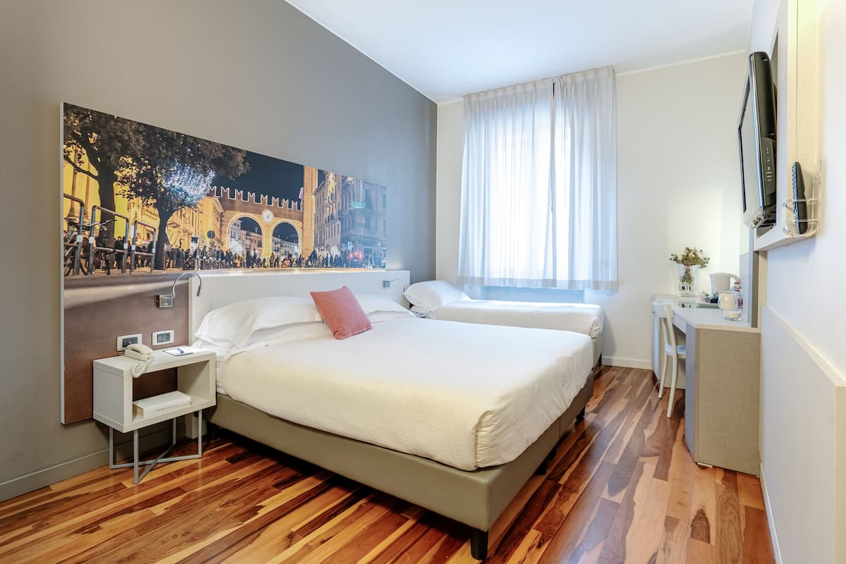 A hotel room with a large bed, a bedside table, a desk, and a chair.