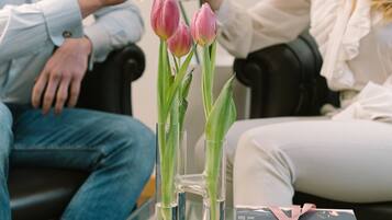 Ein Mann und eine Frau sitzen auf einer Couch, vor ihnen ein Glastisch, eine Vase mit Tulpen und ein verpacktes Geschenk.