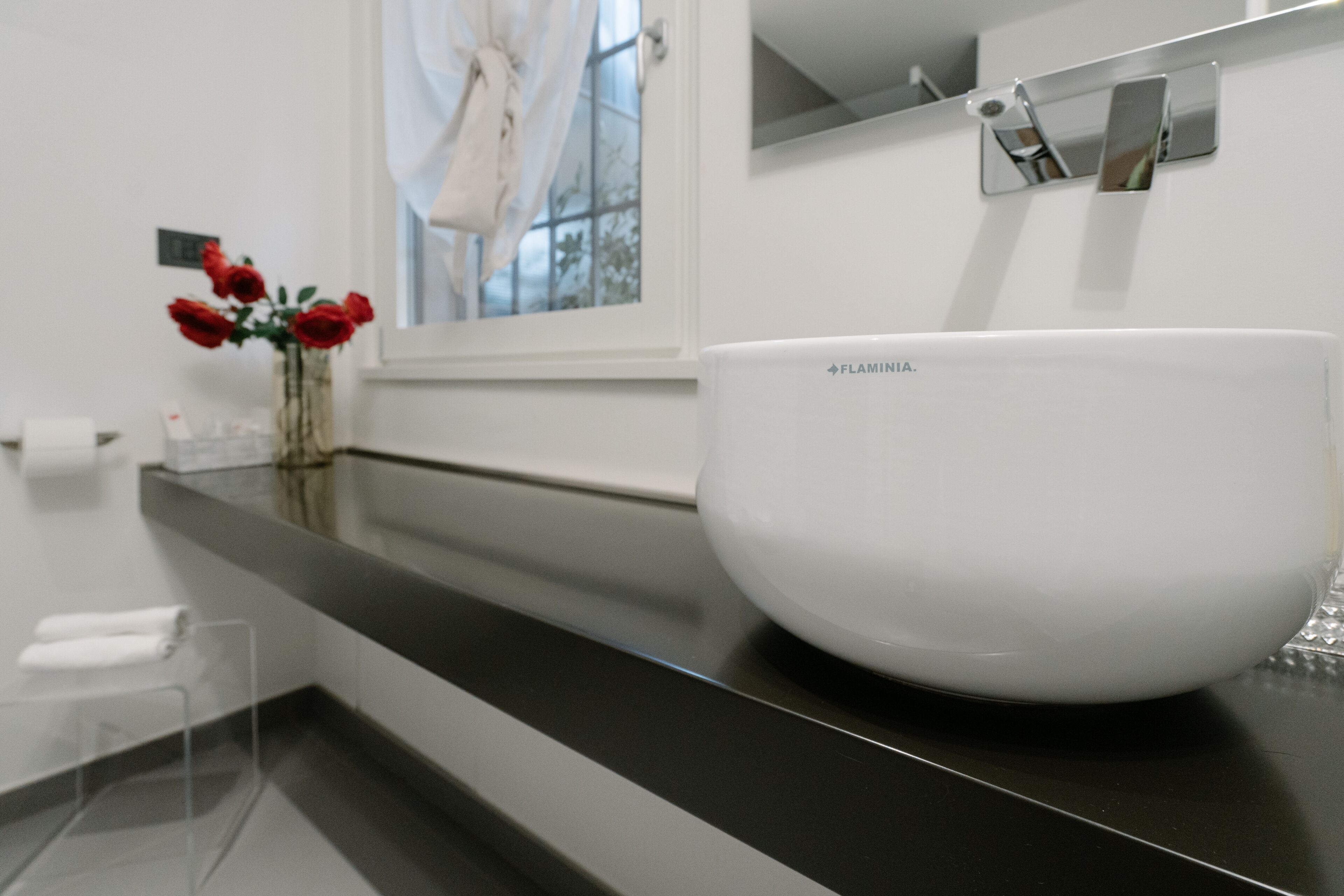 A white basin on a black countertop in a bathroom with a window and a mirror above it.