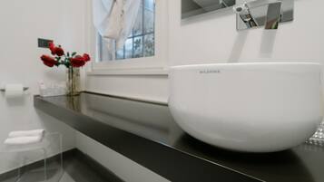 A white basin on a black countertop in a bathroom with a window and a mirror above it.