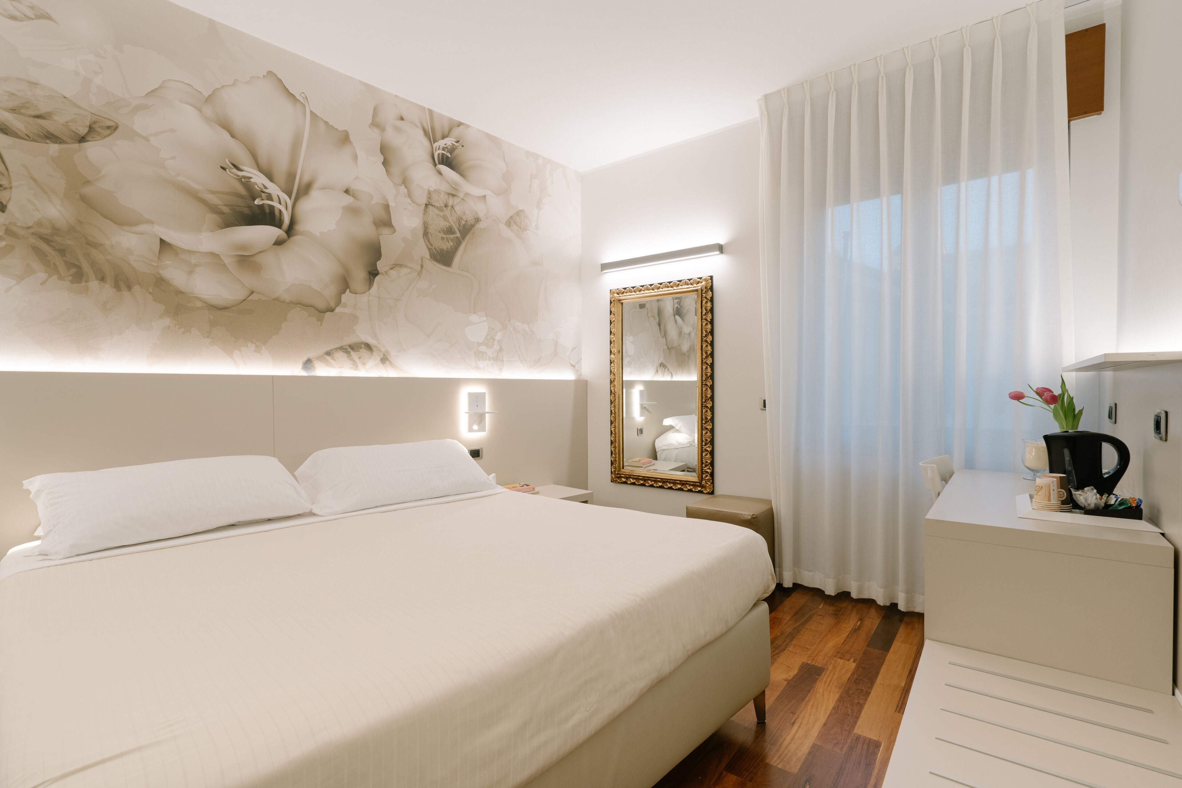 Una camera d'albergo con un letto grande, un comodino, uno specchio e una scrivania con una macchina per il caffè.