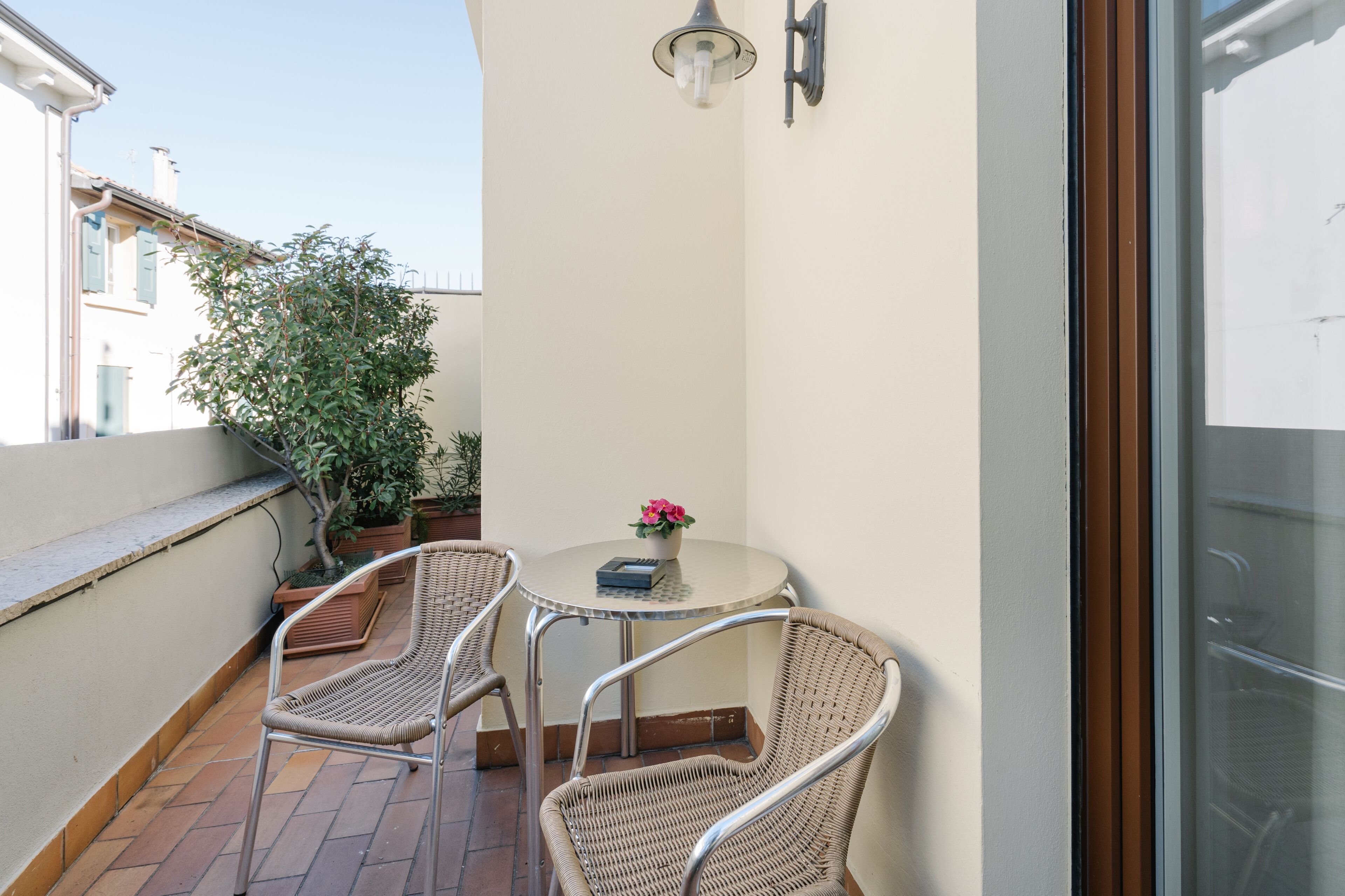 Un petit balcon avec des chaises en osier, une table et un pot de fleurs.