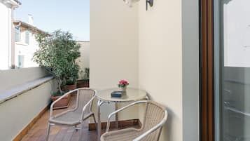 A small balcony with wicker chairs, a table, and a potted plant.