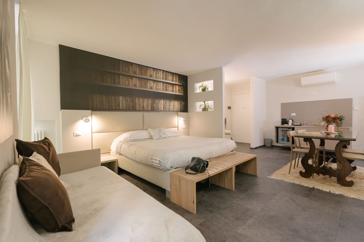 A modern bedroom with a large bed, bedside tables, a wooden bench, a desk, and a bookshelf.