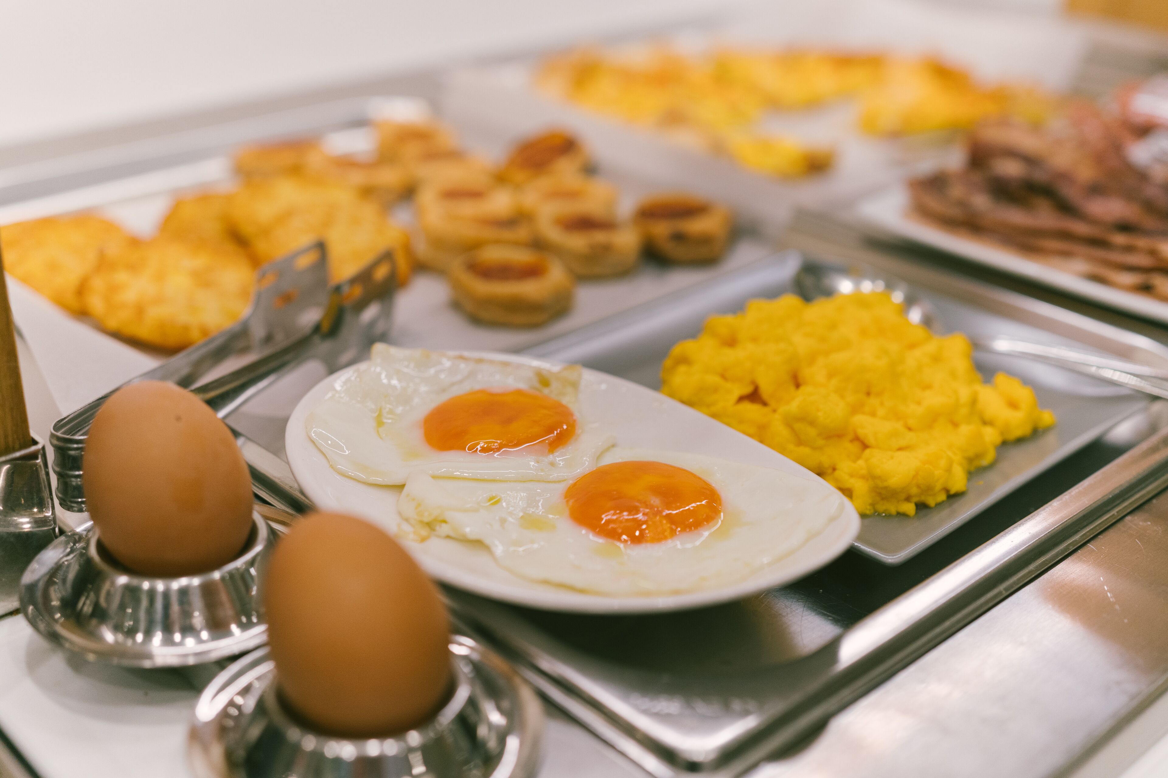 A buffet with various breakfast items including eggs, scrambled eggs, and pastries.