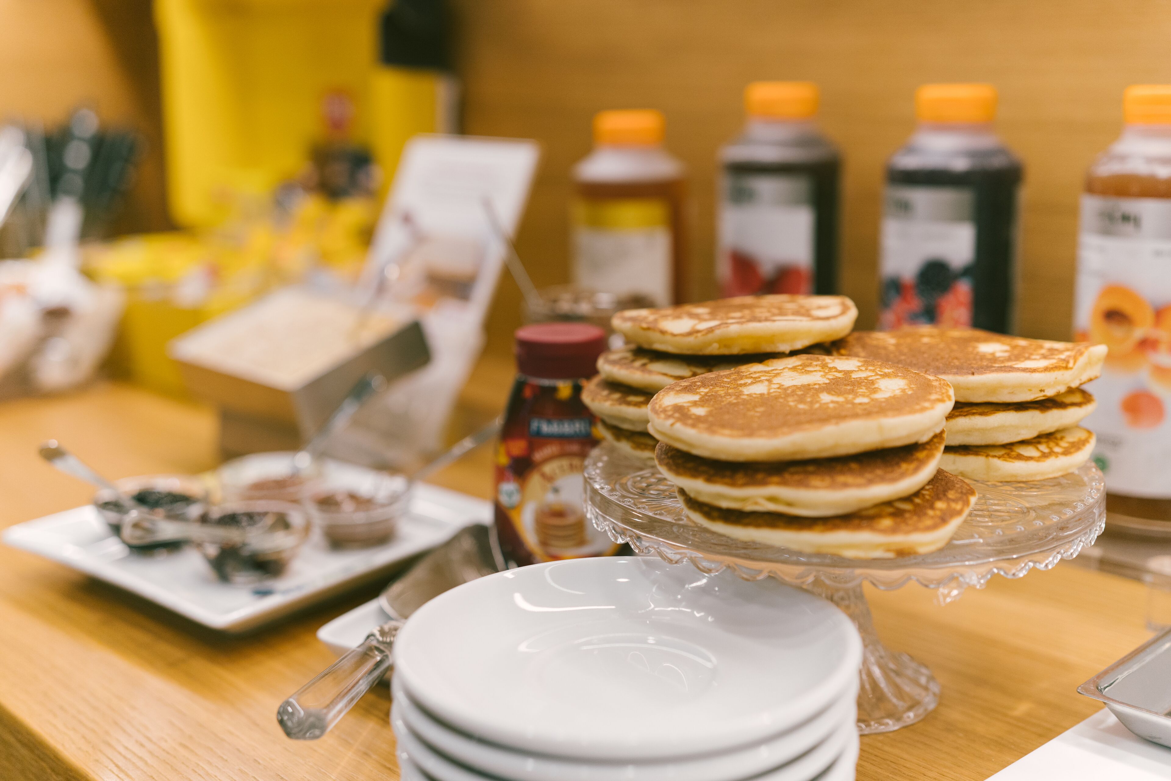 Un bufé de desayuno con panqueques, botellas de jarabe y una estación de café.