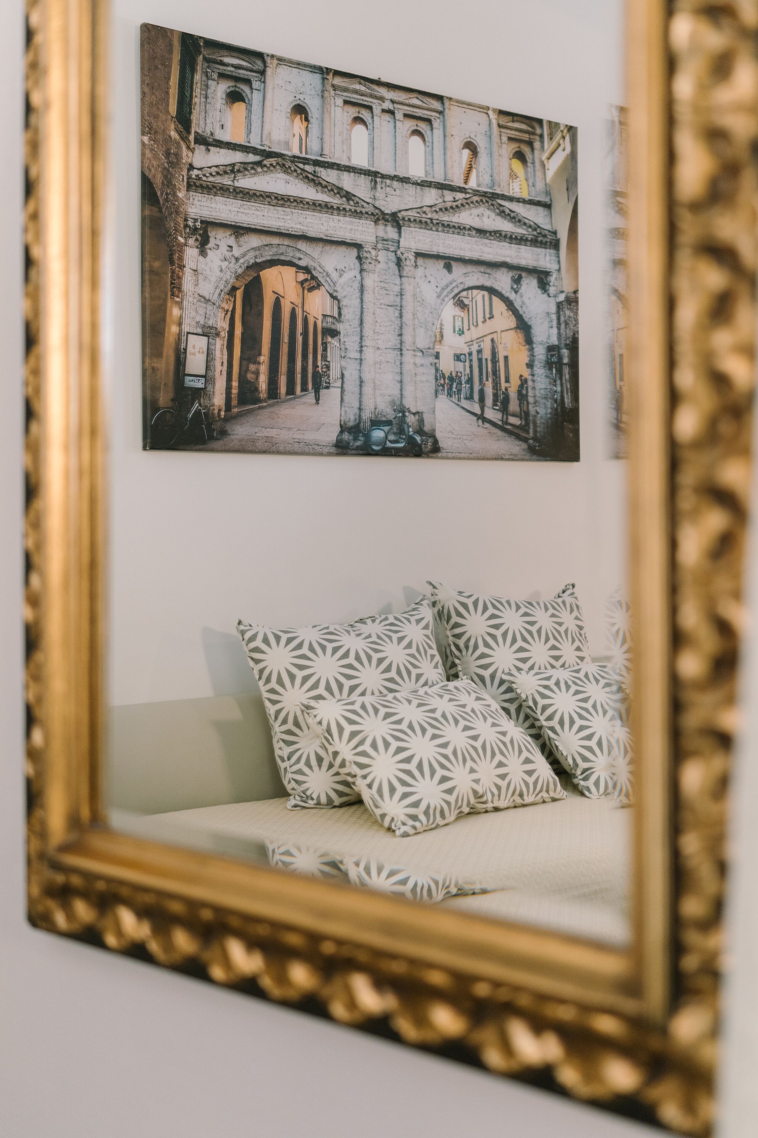 A framed photograph of an architectural structure, a white sofa with patterned cushions, and a gold-framed mirror.