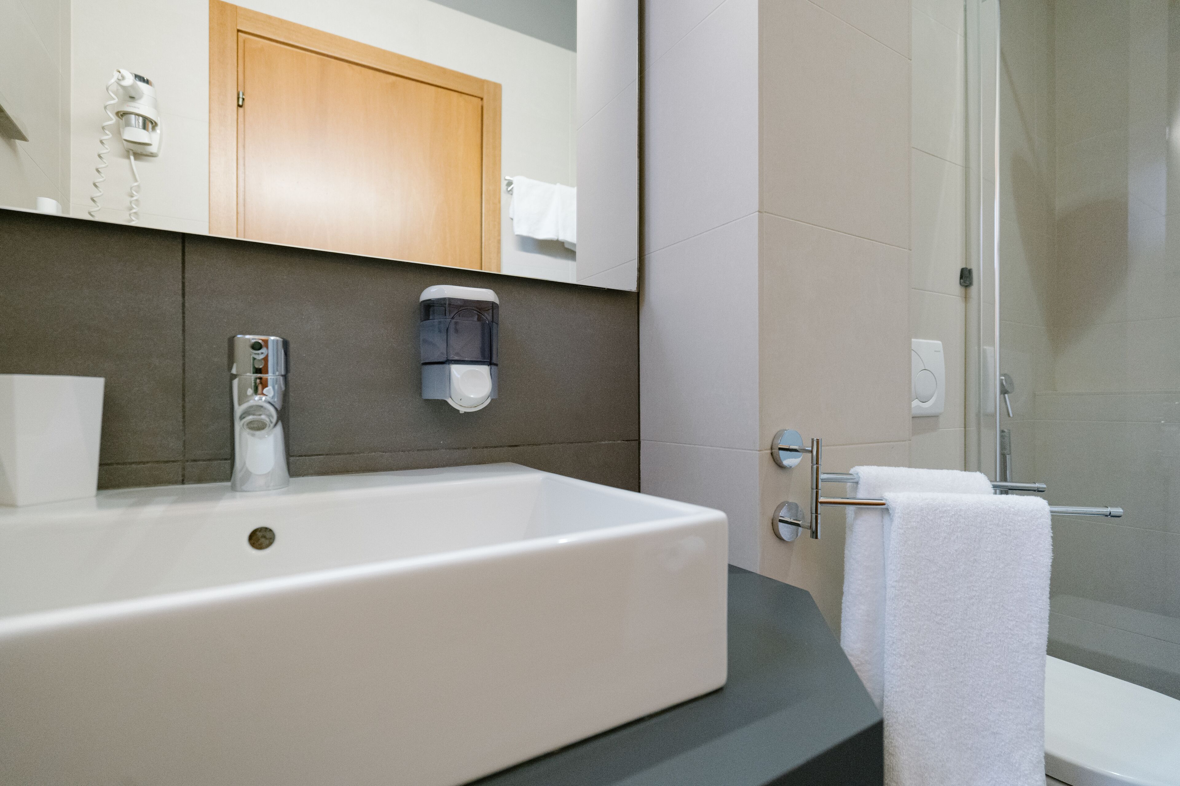 Un baño moderno con un lavabo grande de color blanco, un mueble de madera encima y una mampara de ducha de vidrio.