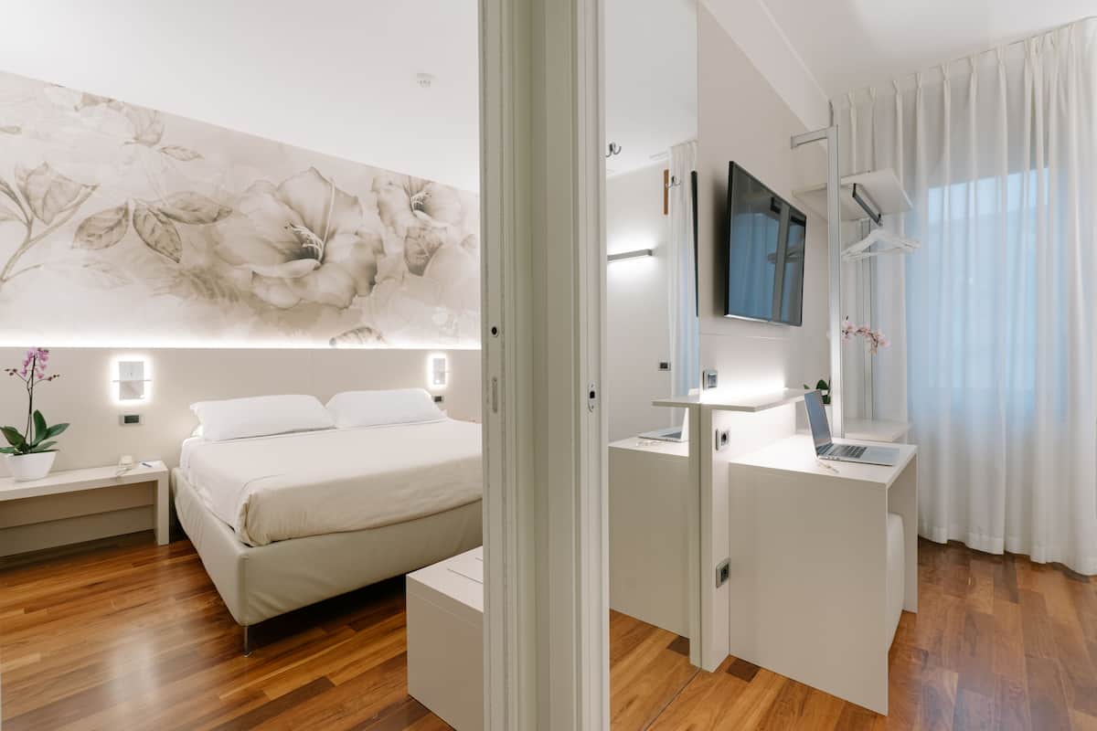 A modern bedroom with a bed, bedside table, and a desk with a TV and lamp.