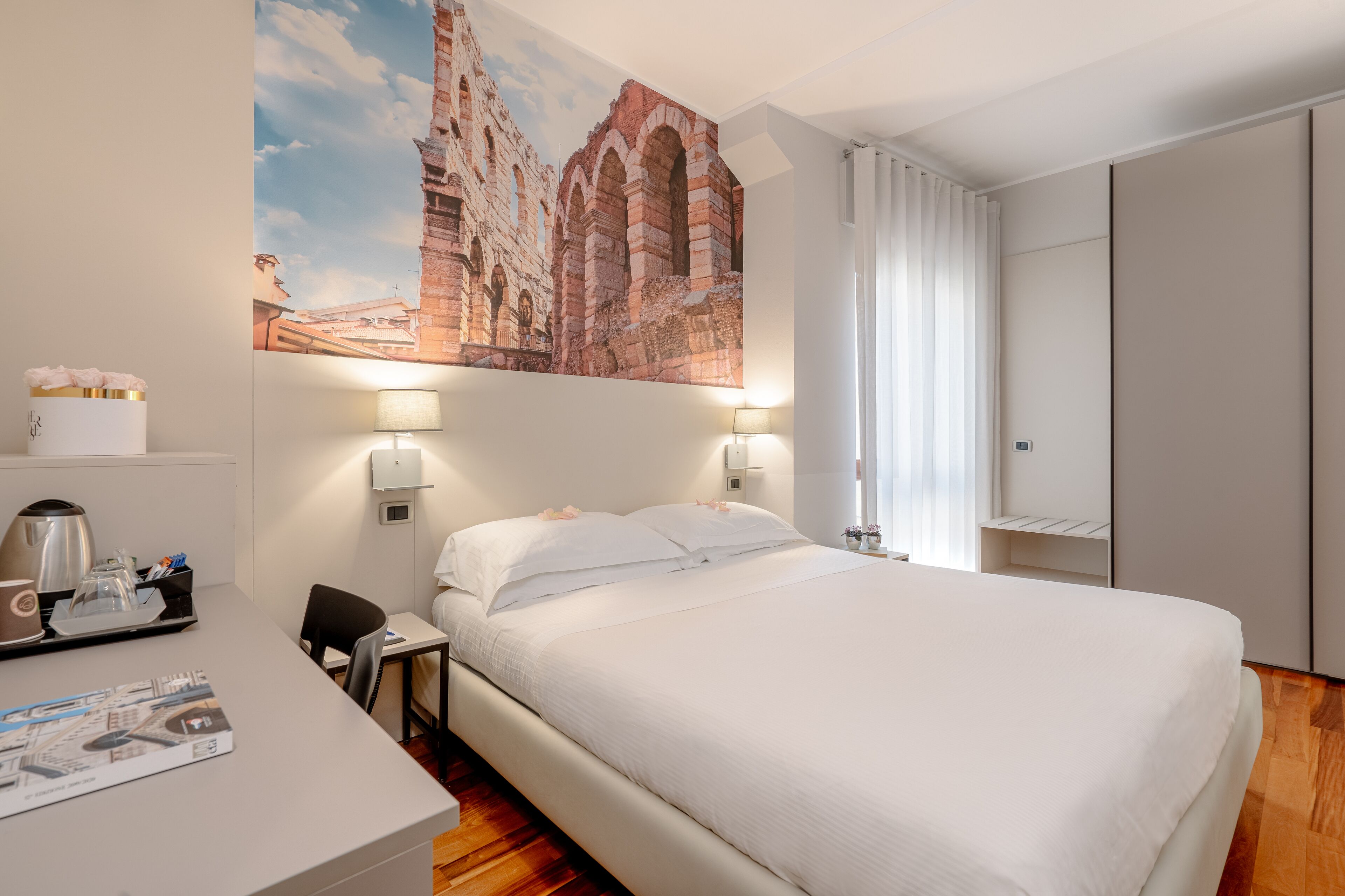 A hotel room with a large bed, two bedside lamps, a desk with a coffee maker, and a bookshelf.