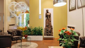 Un área de recepción con una estatua, sillones de cuero, plantas en macetas y una lámpara colgante moderna.