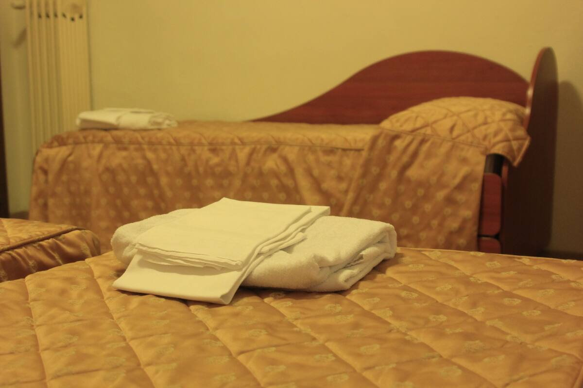 Une chambre d’hôtel avec un lit bien fait, une tête de lit en bois et une fenêtre avec des stores.