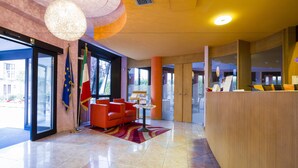 A lobby with a reception desk, a chandelier, and flags. - Hotel Sirena (Cesenatico)