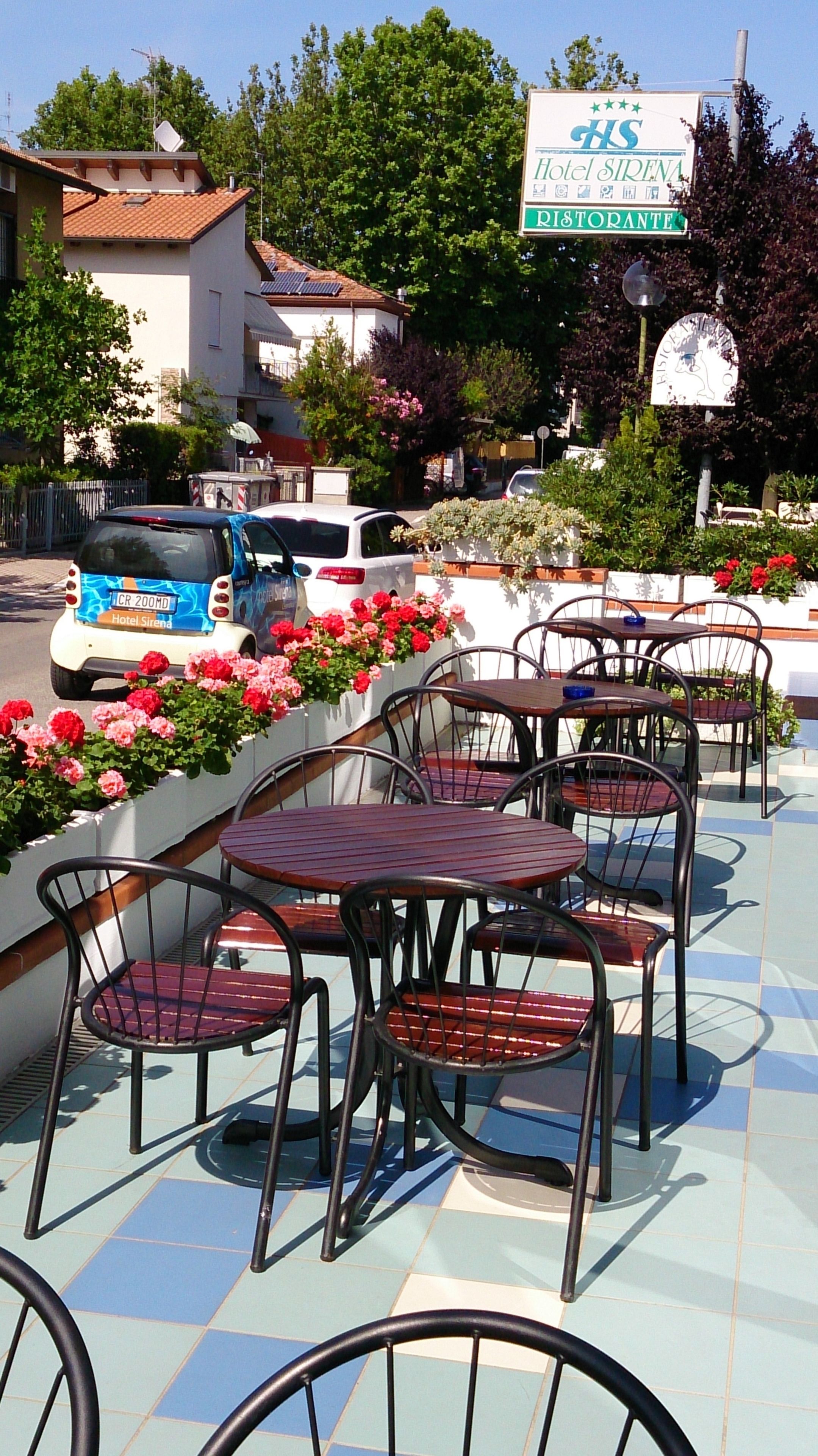 Outdoor seating with metal chairs and tables, a sign for Hotel Sirena Ristorante, and a parked car.