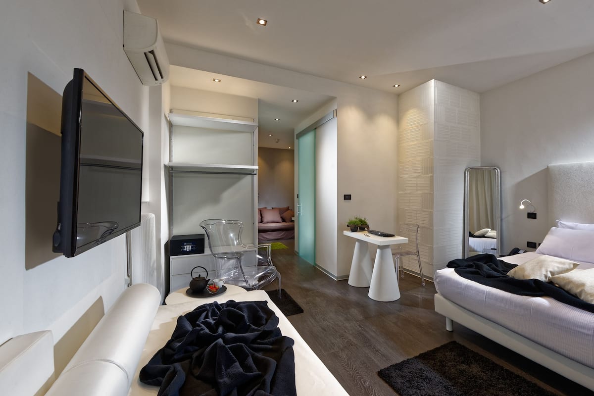 Ein modernes Hotelzimmer mit Flachbildfernseher, einem großen Bett, einem Nachttisch mit Lampe und einem begehbaren Kleiderschrank.