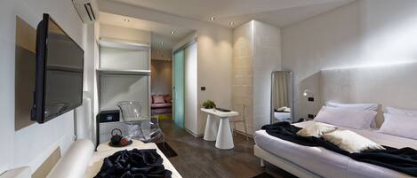 A modern hotel room with a flat-screen TV, a large bed, a bedside table with a lamp, and a walk-in closet.