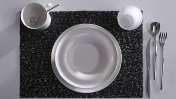 Une table dressée avec une assiette blanche, une tasse blanche, une cuillère, une fourchette et un couteau, le tout posé sur une nappe noire à texture.