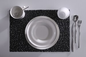 Une table dressée avec une assiette blanche, une tasse blanche, une cuillère, une fourchette et un couteau, le tout posé sur une nappe noire à texture.