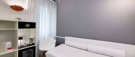 Et moderne hotelværelse med seng, skrivebord med computer, stol og et lille bord med et bakke med småkager.