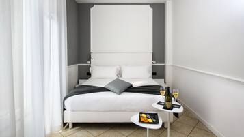A modern hotel room with a large bed, a small table with a bottle and glasses, and a neatly made bed with pillows.