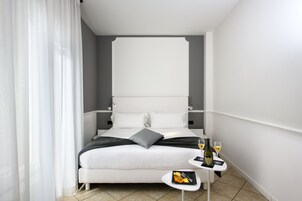 A modern hotel room with a large bed, a small table with a bottle and glasses, and a neatly made bed with pillows.