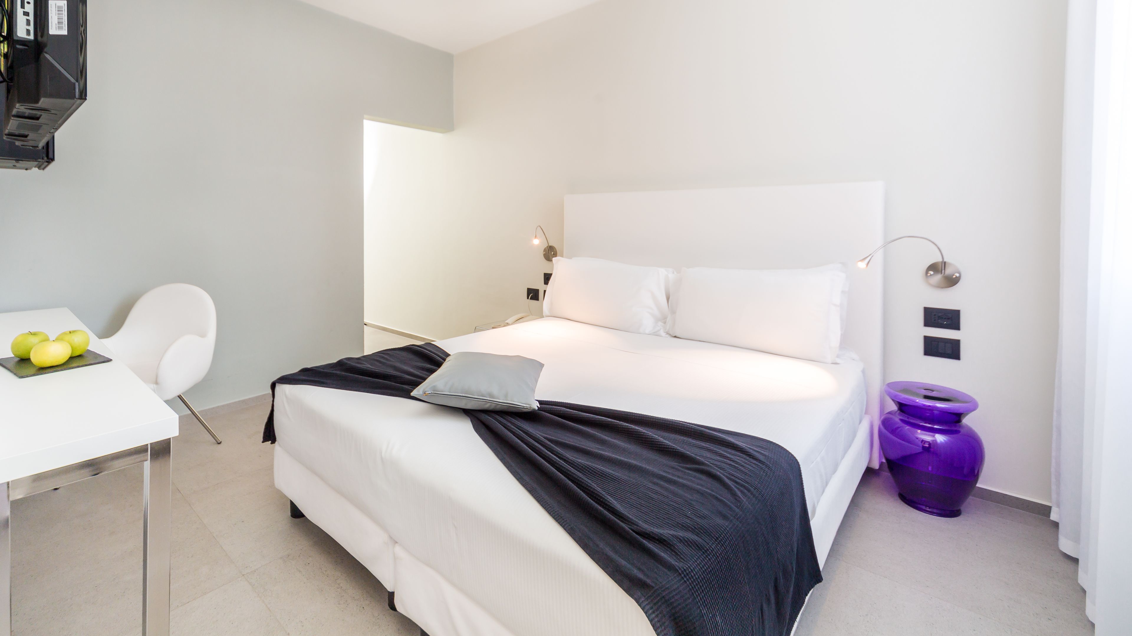 A modern hotel room with a large bed, a desk with a laptop, and a chair.