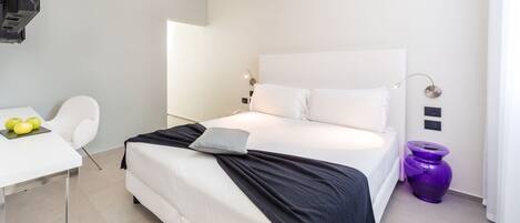 A modern hotel room with a large bed, a desk with a laptop, and a chair.