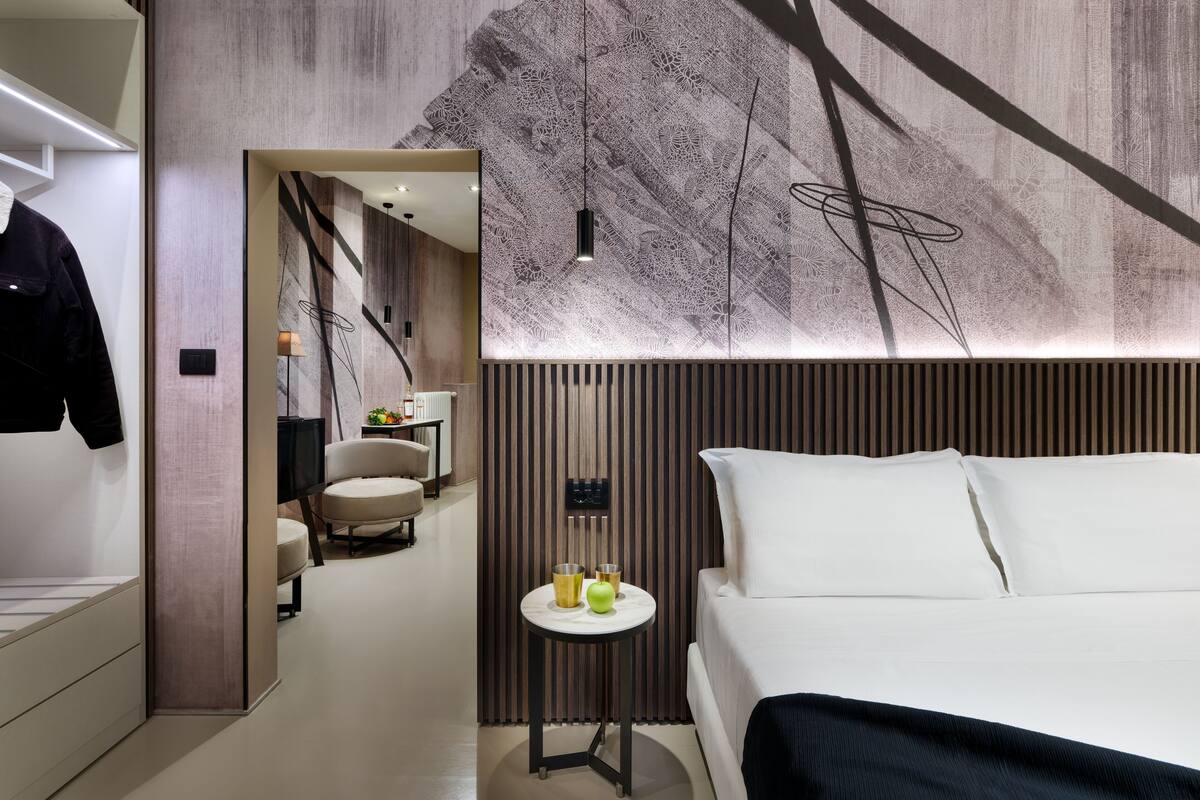 Ein modernes Hotelzimmer mit Bett, einem kleinen Tisch mit Lampe sowie einer Wand mit dekorativem Muster.