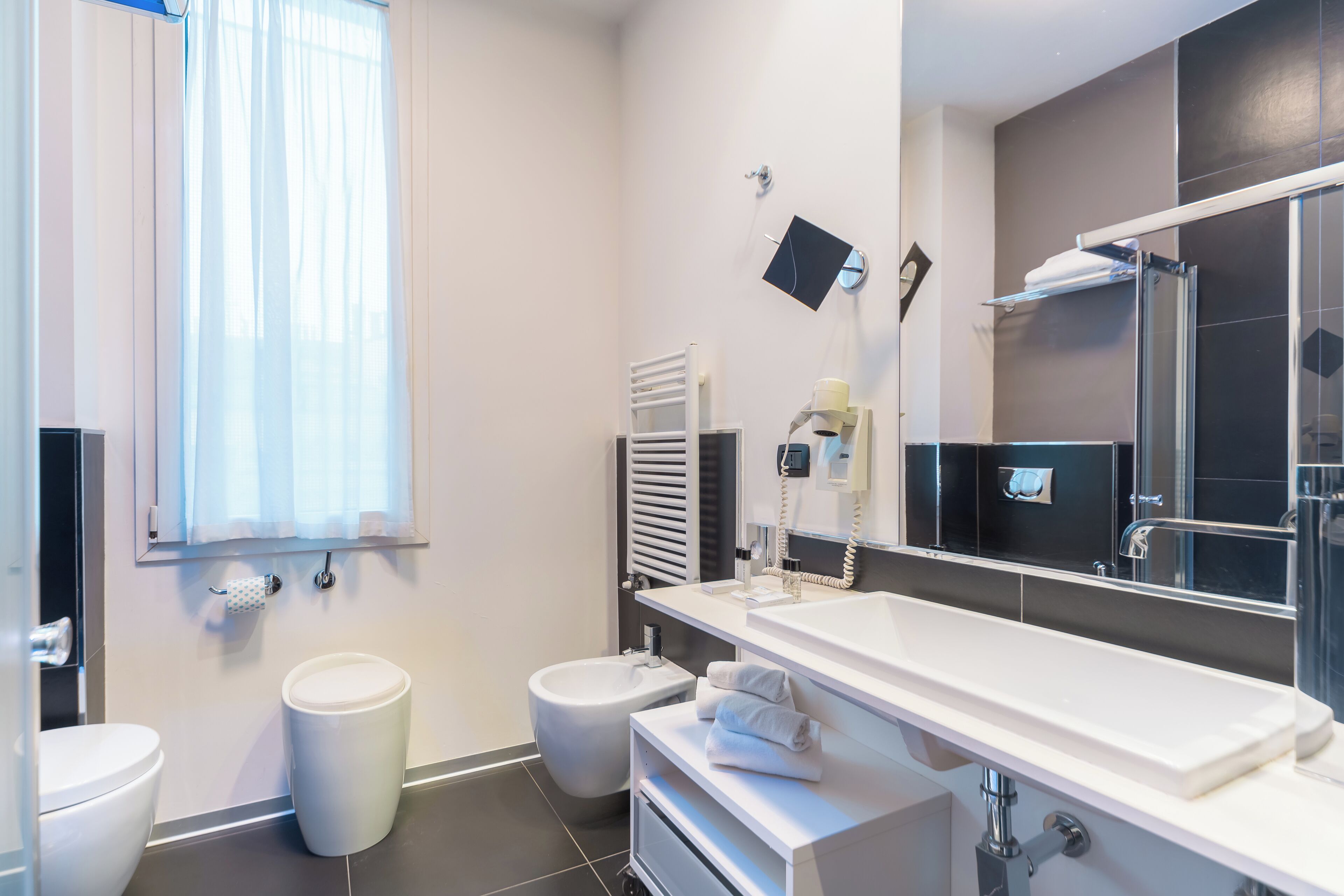 Un bagno moderno con il water, un bidet, un lavandino e un grande specchio.