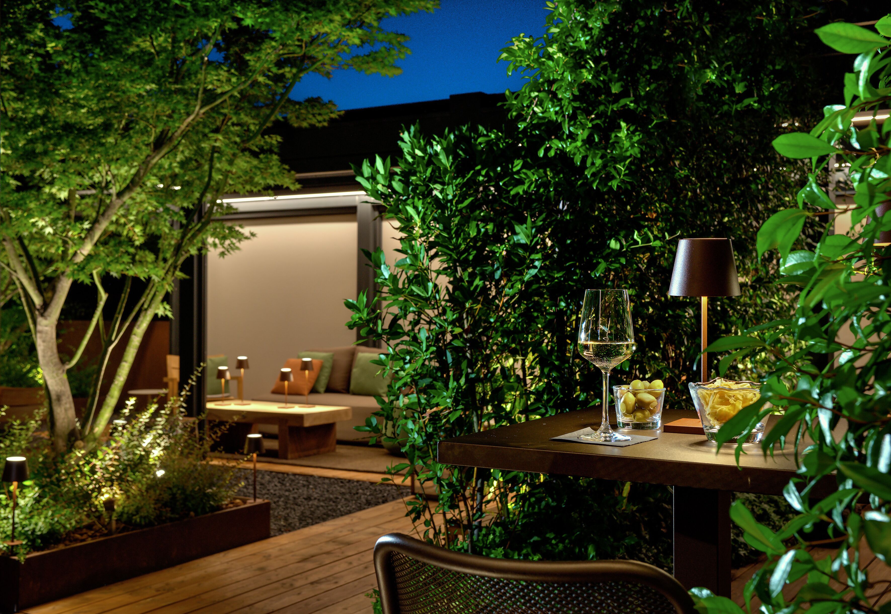 An outdoor patio area with a table set for dining, surrounded by lush greenery and a cozy seating area.