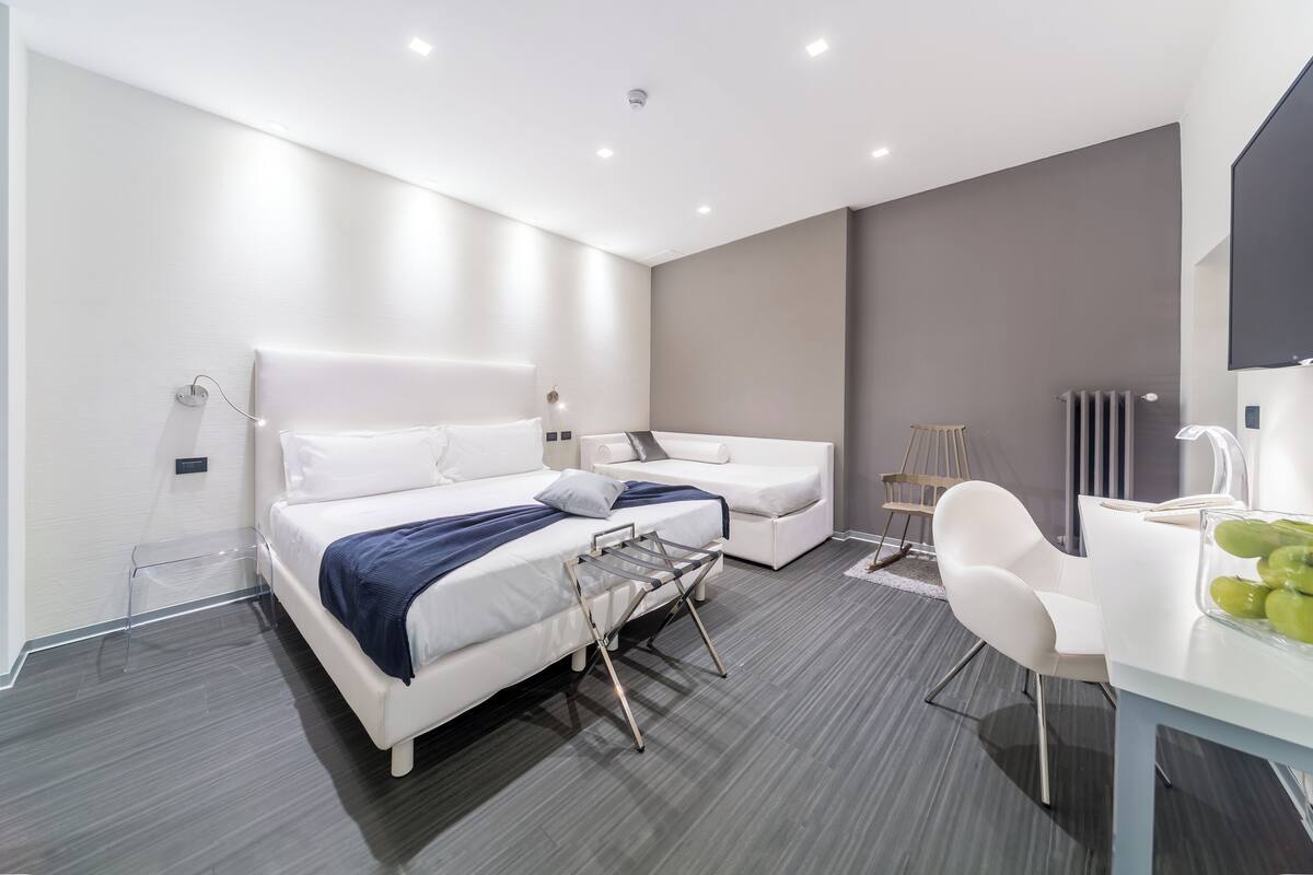 Ein modernes Hotelzimmer mit einem Bett, einer Couch, einem Sessel und einem Tisch mit Obst.