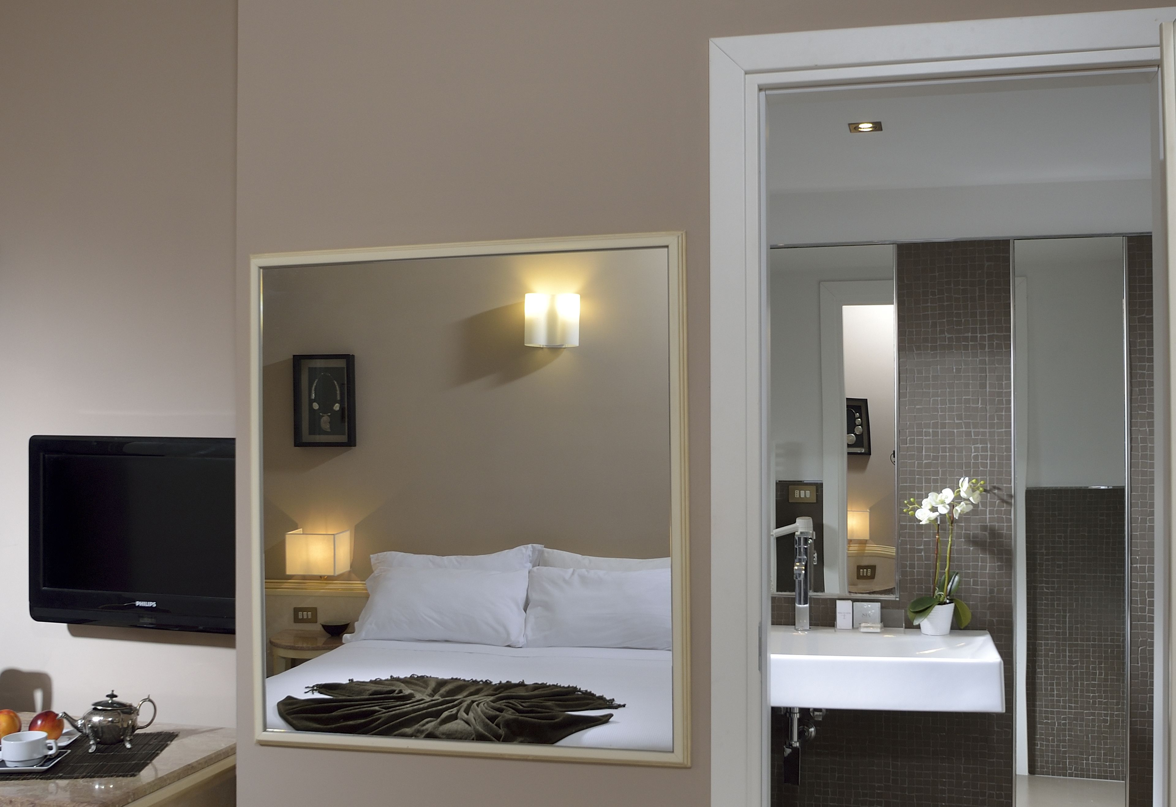 Habitación de hotel con cama, lámpara de noche, televisor y baño con lavamanos y espejo.